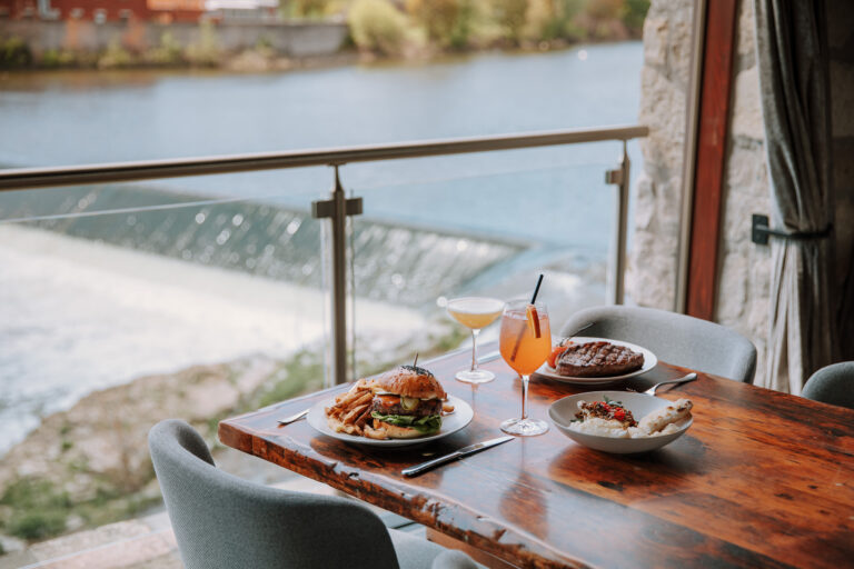 A burger and steak on a table next to the waterfront at Cambridge Mill